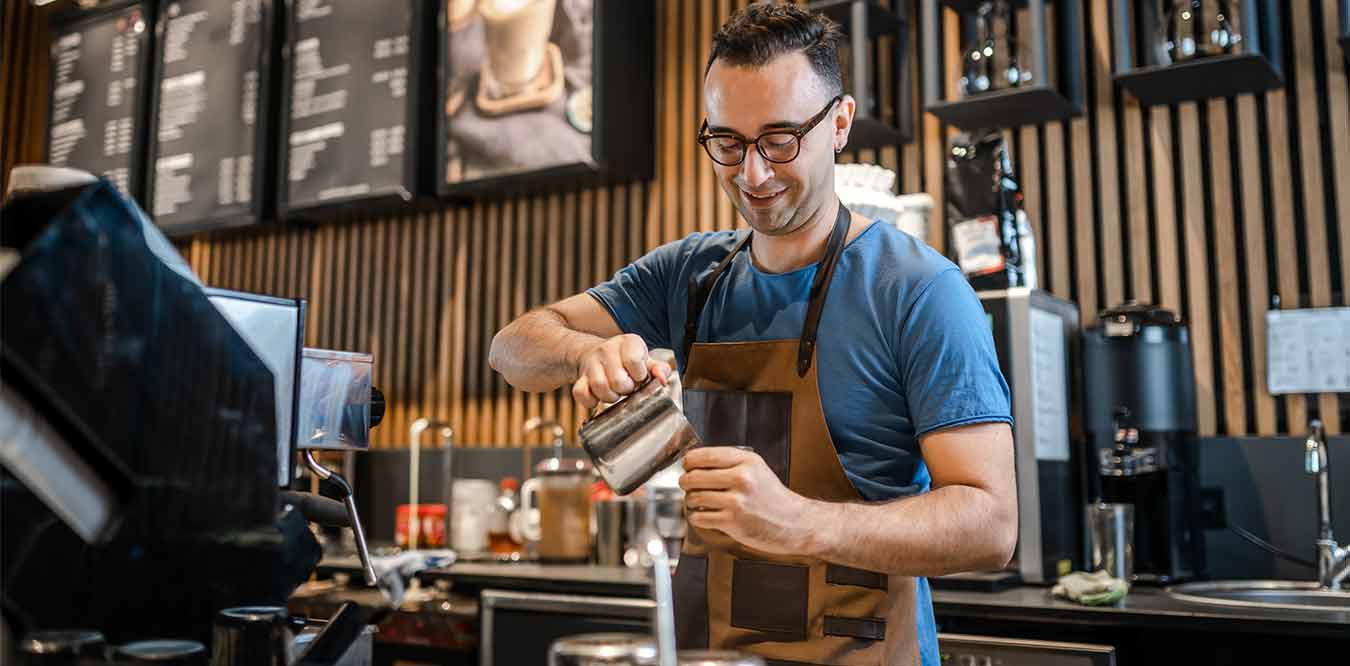 Male barista making coffee for customers at coffee station
